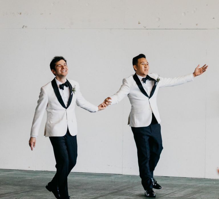 Grooms in matching outfits entering their industrial wedding reception