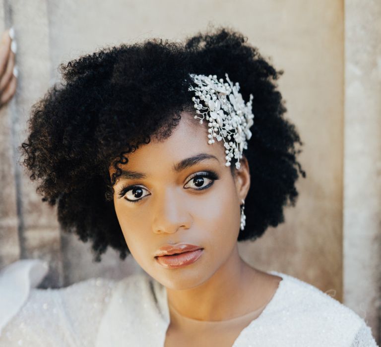 Black Bride with Afro Hair Wearing an Ornate Pearl Hair Accessory and Shimmering Emma Beaumont Wedding Dress