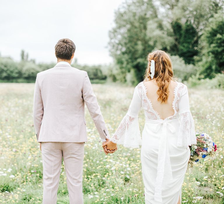 Groom in pink suit and bride in bell sleeve dress in a meadow