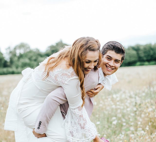 Bride jumping on her grooms back in a summer meadow