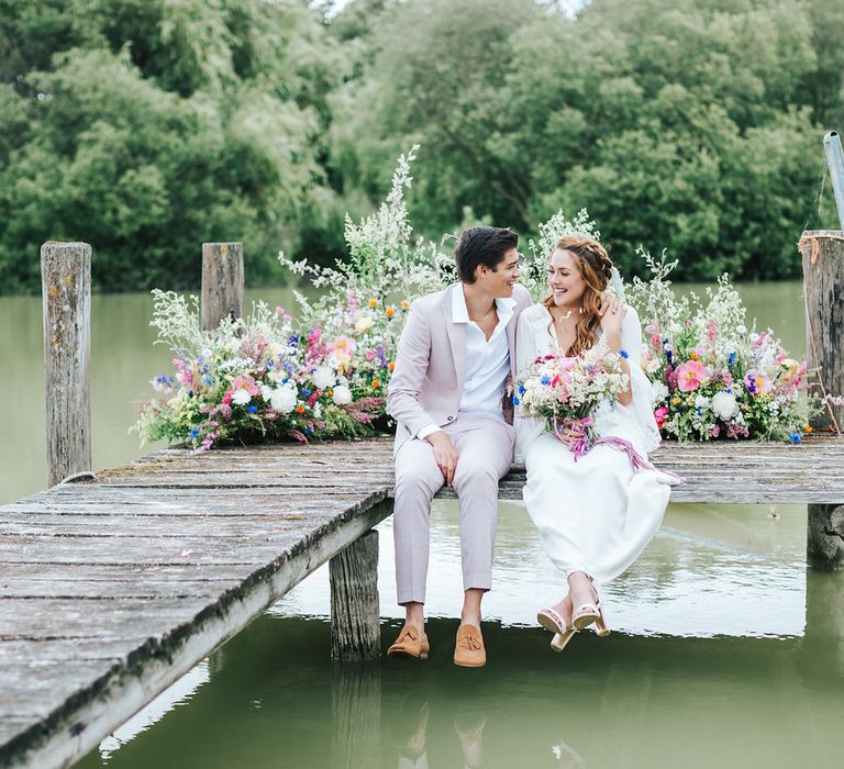 Bride and groom sitting on the dock at Summer wedding