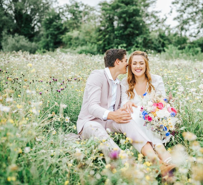 Boho bride and groom sitting in a flower filled meadow