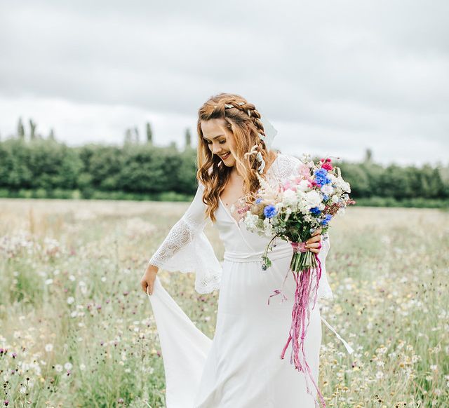 Boho bride with braid and bell sleeve wedding dress in a meadow