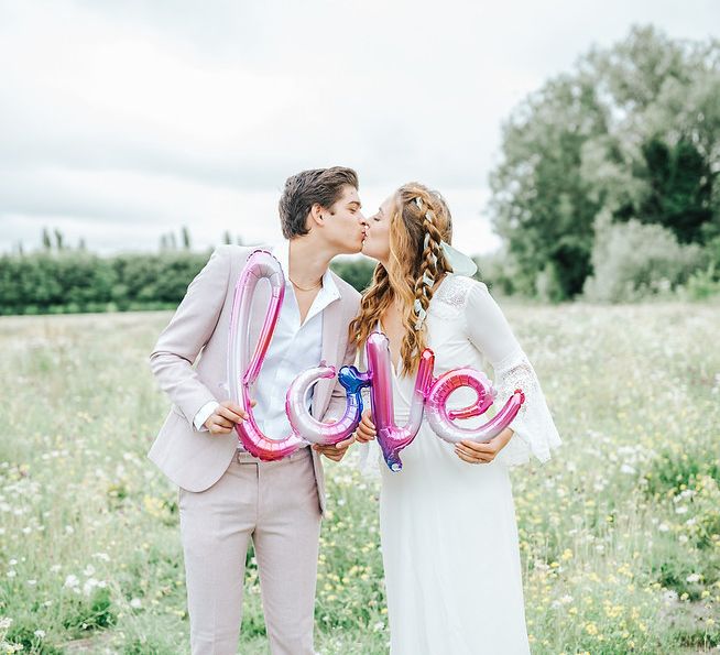 Bride and groom holding a pink foil LOVE balloon  - wedding ideas for summer