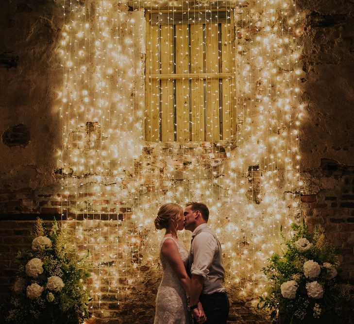 Bride and Groom Kissing in Front of Fairy Light Backdrop