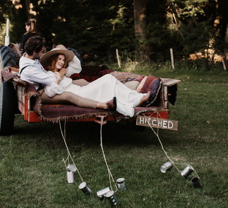 Boho bride and groom sitting not he back of a trailer pulled by a tractor