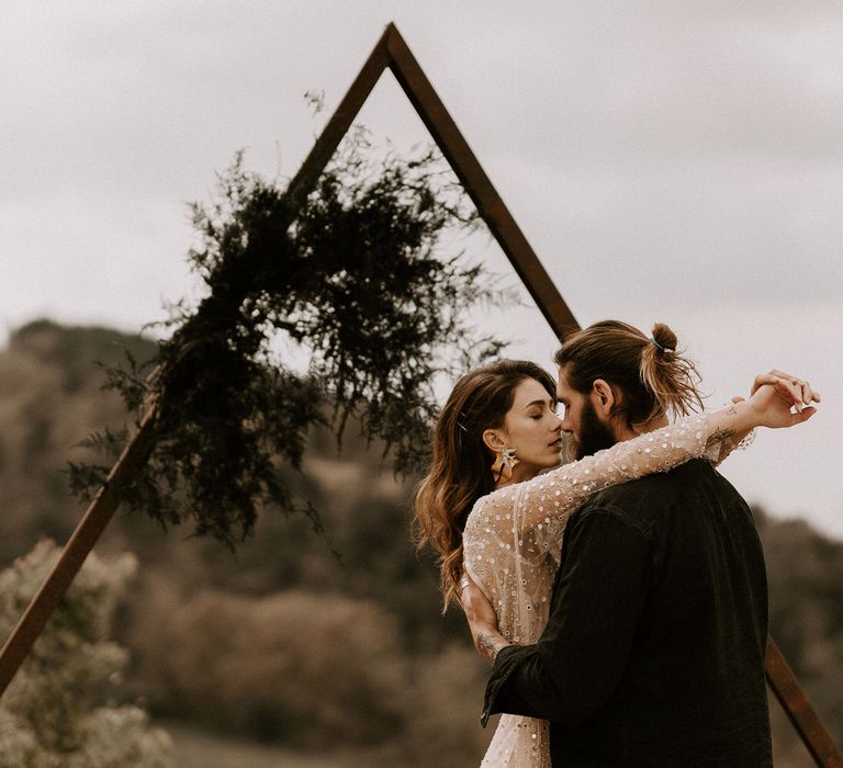 Bride in Gold Shimmering Wedding Dress Embracing Groom in Black Suit with Top Knot