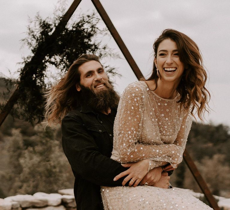 Bearded Groom in Black Outfit Picking Up his Bride in Shimmering Gold Wedding Dress