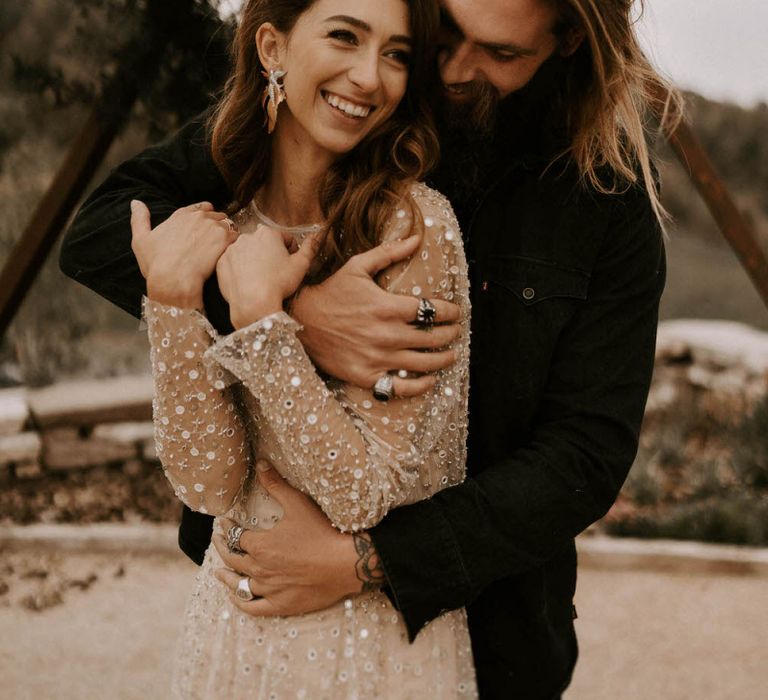 Bearded Groom in Black Outfit Embracing his Bride in Shimmering Gold Wedding Dress