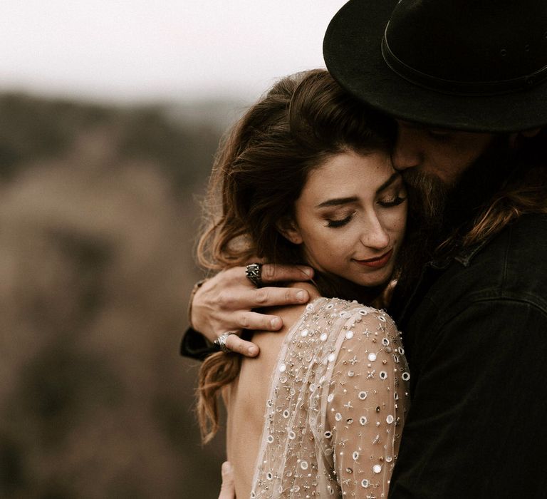 Bride in Sparkly Gold Wedding Dress and Groom in Black Fedora Hat Embracing