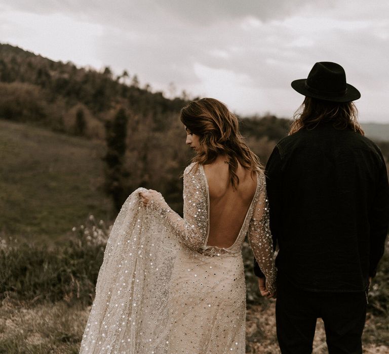 Bride in Backless Gold Sequin Wedding Dress and Groom in Black Fedora Hat Overlooking The Spanish Mountains