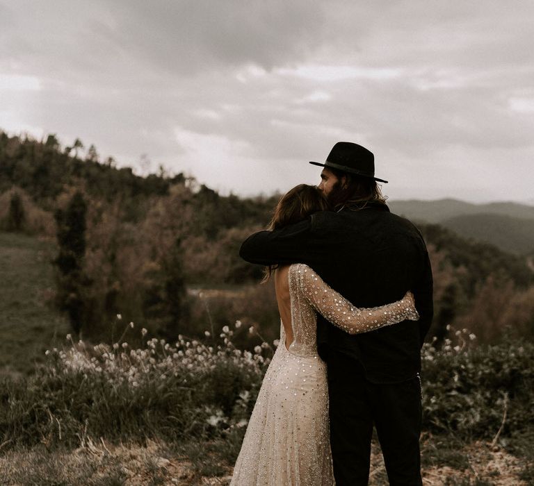 Bride in Backless Gold Sequin Wedding Dress and Groom in Black Fedora Hat Embracing