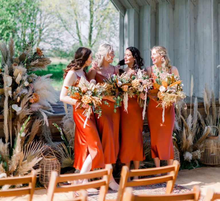 Bridesmaids in Burnt Orange Bridesmaids Dresses with Dried Flower Bouquets Standing in Front of the Wooden Ceremony Hut