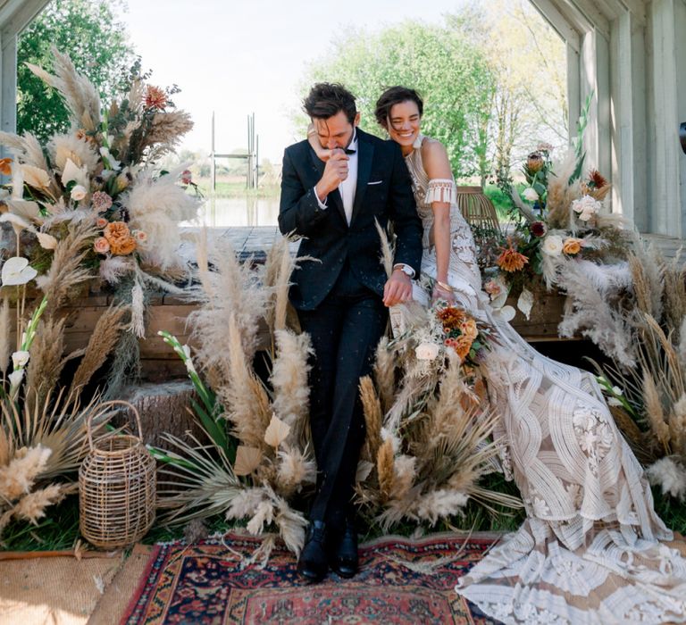 Bride in Rue De Seine Boho Wedding Dress and Groom in Black Tie Laughing at their Ceremony Altar