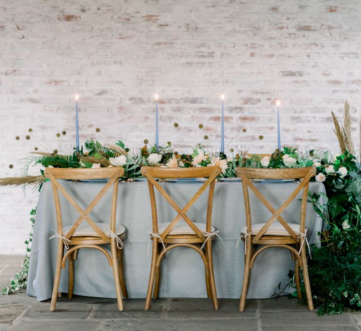 Winter Wedding Table with Wooden Chairs, Blue Linen and Foliage Filled Flower Arrangements