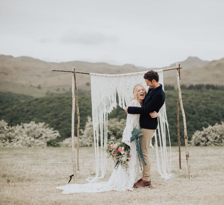 Groom in Navy Blazer and Beige Chinos Embracing His Boho Bride in a Lace Wedding Dress