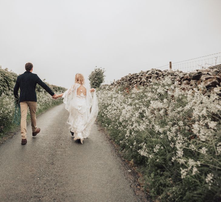 Groom in Beige Chinos and Navy Blazer Walking With His Bride in a Lace Rue de Seine Wedding Dress