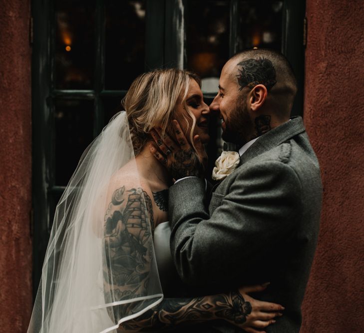 Tattooed Bride with Sweetheart Wedding Dress and Groom in Highland Wear Embracing Her Face