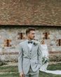 Portrait of the groom in a grey three-piece wedding suit with his bride in the background