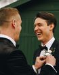 groom and his best man wearing black tie wedding suits while best man helps groom with buttonhole