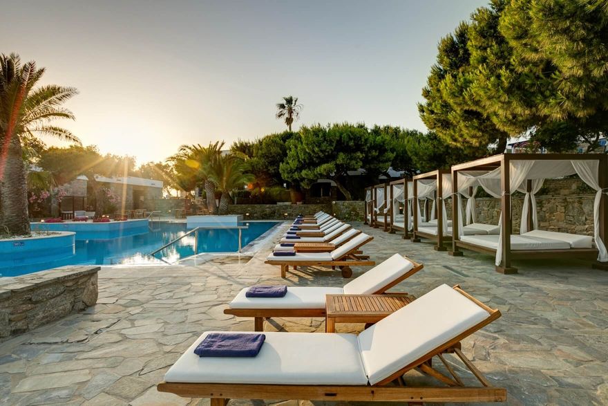Mykonos Theoxenia Hotel pool with sun loungers and luxury cabanas surrounded by palm trees and stone paths