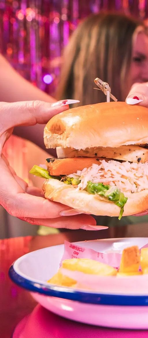 Woman holding a burger with chips and prosecco at the Tonight Josephine bottomless brunch in Birmingham