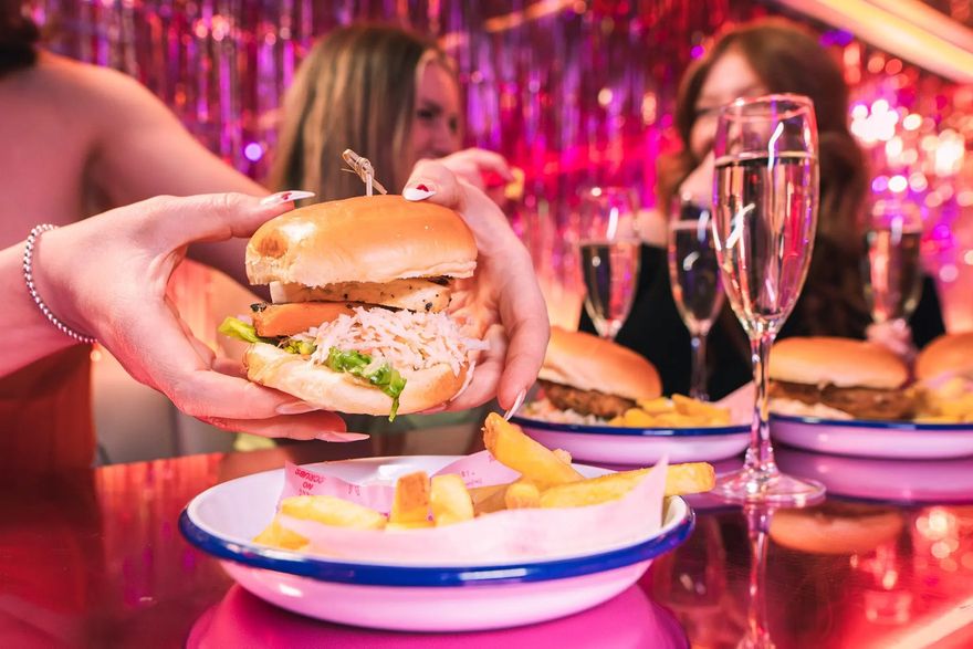 Woman holding a burger with chips and prosecco at the Tonight Josephine bottomless brunch in Birmingham