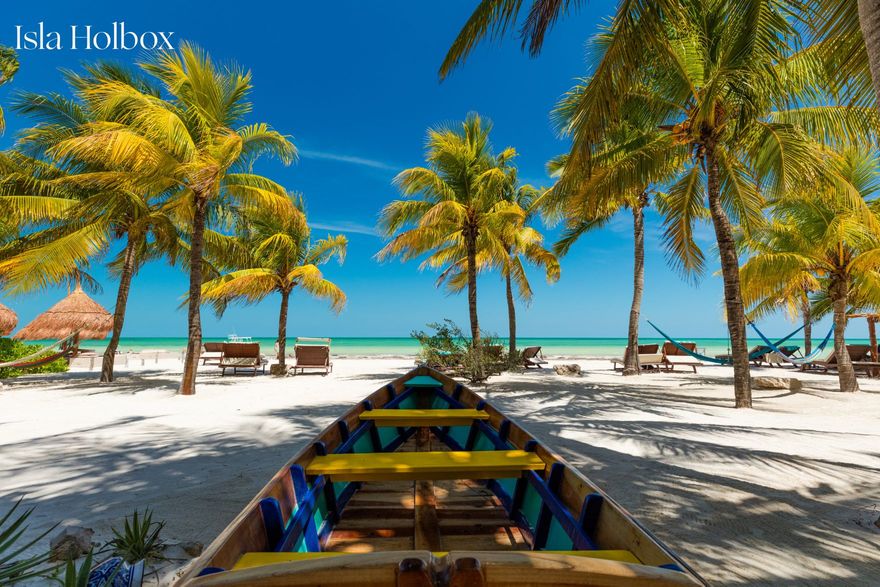 Palm tree lined beach with blue skies and wooden boat for beach honeymoon in Isla Holbox, Mexico
