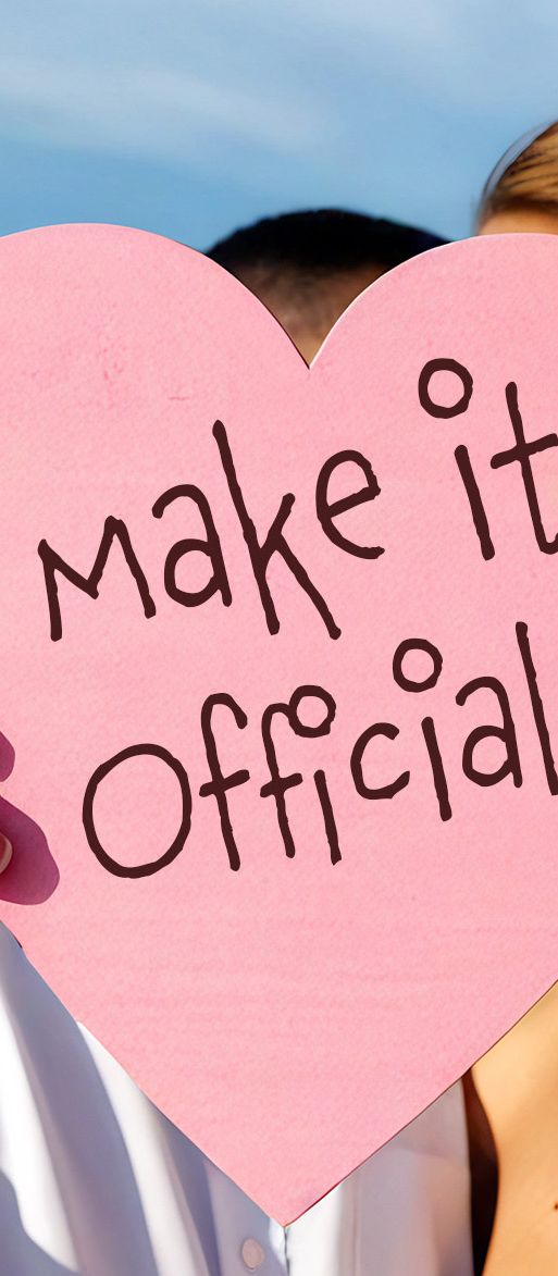 couple holding up 'make it official' sign on a beach wedding 