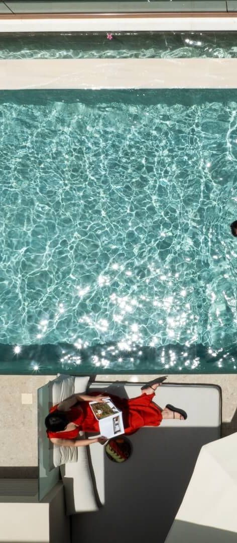 Aerial view of a couple enjoying a private swim-up suite at Asterion Suites & Spa in Crete, featuring a luxury pool, sun lounger and contemporary outdoor terrace.