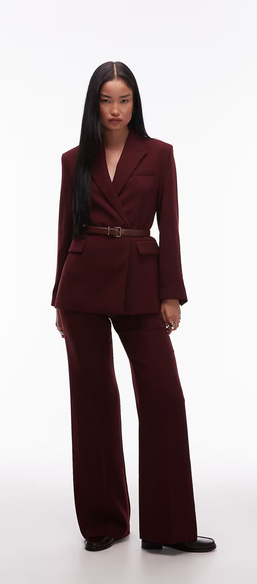 Model wearing a burgundy belted blazer and matching wide-leg trousers against a pale backdrop