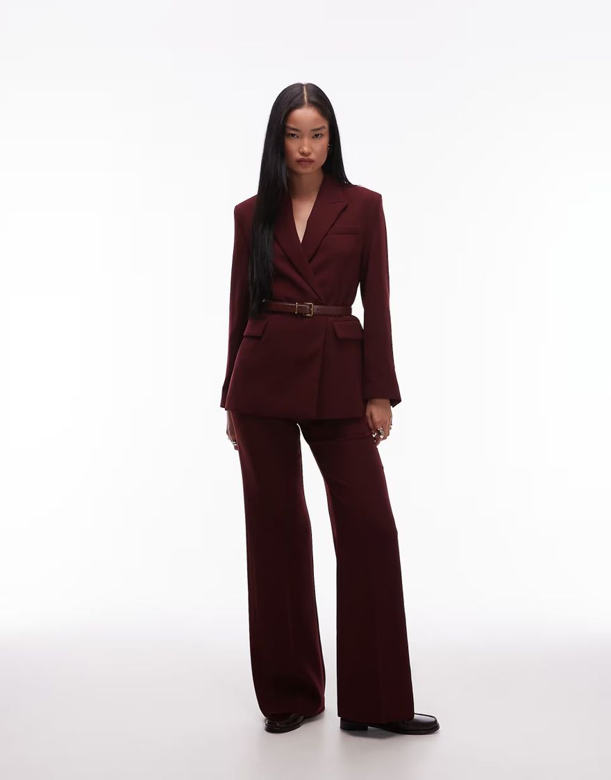 Model wearing a burgundy belted blazer and matching wide-leg trousers against a pale backdrop