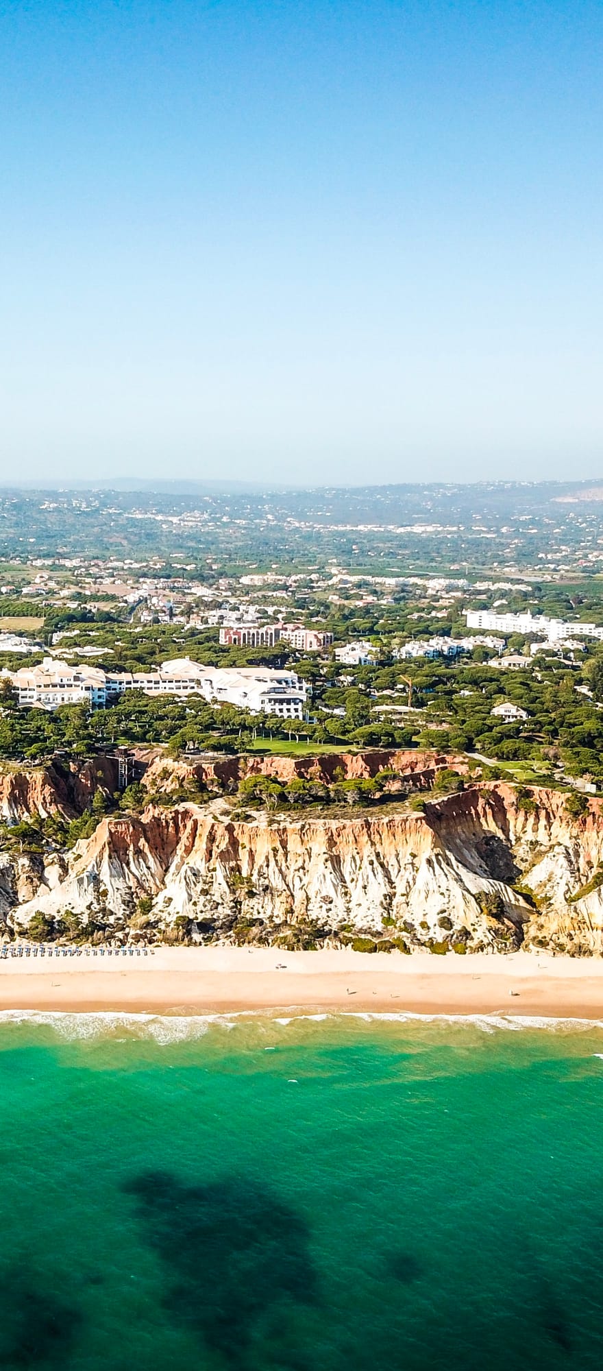 Aerial view of Pine Cliffs Resort overlooking Praia da Falésia beach in the Algarve, Portugal, featuring dramatic red and golden cliffs, turquoise Atlantic waters and a long stretch of sandy coastline.
