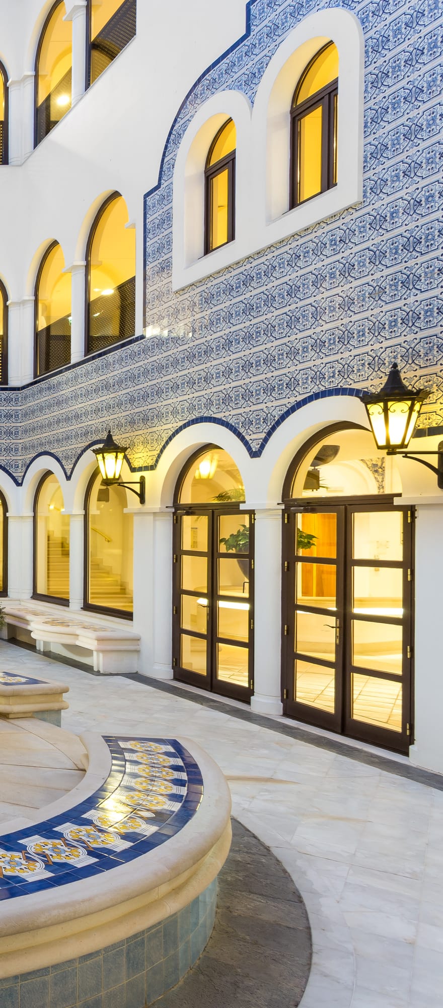 Elegant courtyard at Pine Cliffs Resort in the Algarve, Portugal, featuring traditional blue and white Portuguese tiles, illuminated archways and a central fountain.