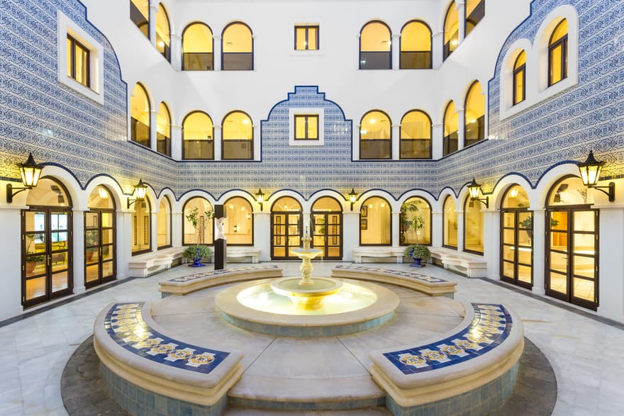 Elegant courtyard at Pine Cliffs Resort in the Algarve, Portugal, featuring traditional blue and white Portuguese tiles, illuminated archways and a central fountain.