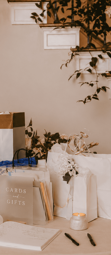 Cards and gifts table with white welcome sign beneath a floral-adorned staircase